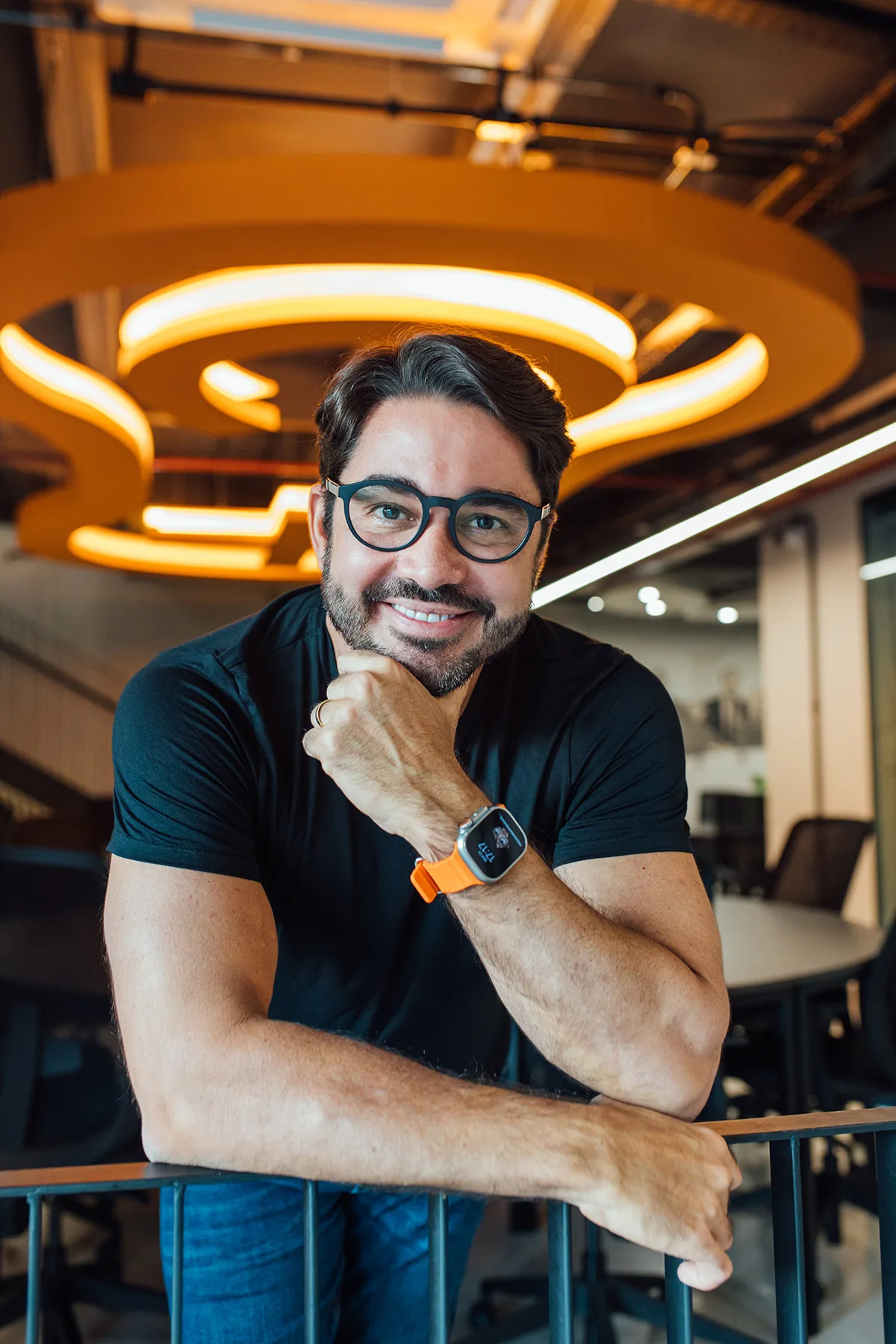 Marcelo Albuquerque sorrindo, apoiado em um corrimão em um espaço de escritório moderno